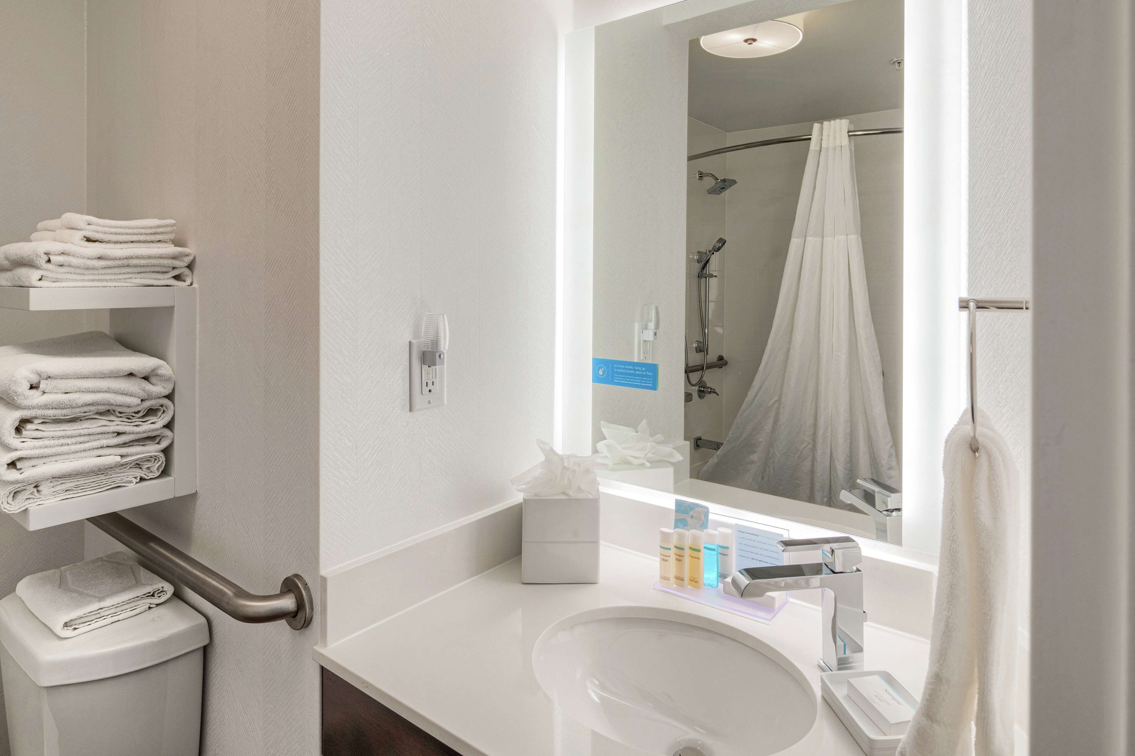 A modern bathroom with a white sink, a mirror, a towel rack, and a shower curtain.