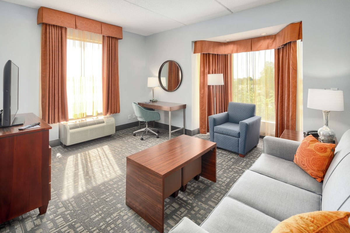 A hotel room with a desk, two chairs, a sofa, a TV, and a lamp.