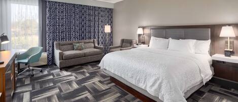 Una habitación de hotel con una cama grande, dos sillones, un escritorio y una silla.
