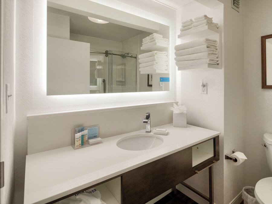 A modern bathroom with a large mirror, white sink, and neatly stacked towels.