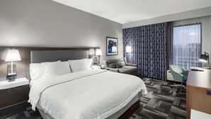 Une chambre d’hôtel avec un grand lit, un bureau, une chaise, un canapé et un rideau à motifs.