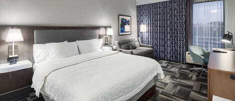 Habitación de hotel con una cama grande, un escritorio, una silla, un sofá y una cortina estampada.
