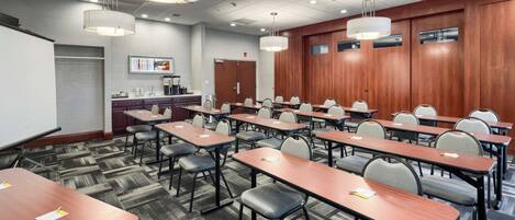 A conference room with multiple tables and chairs, a whiteboard, and a coffee station.