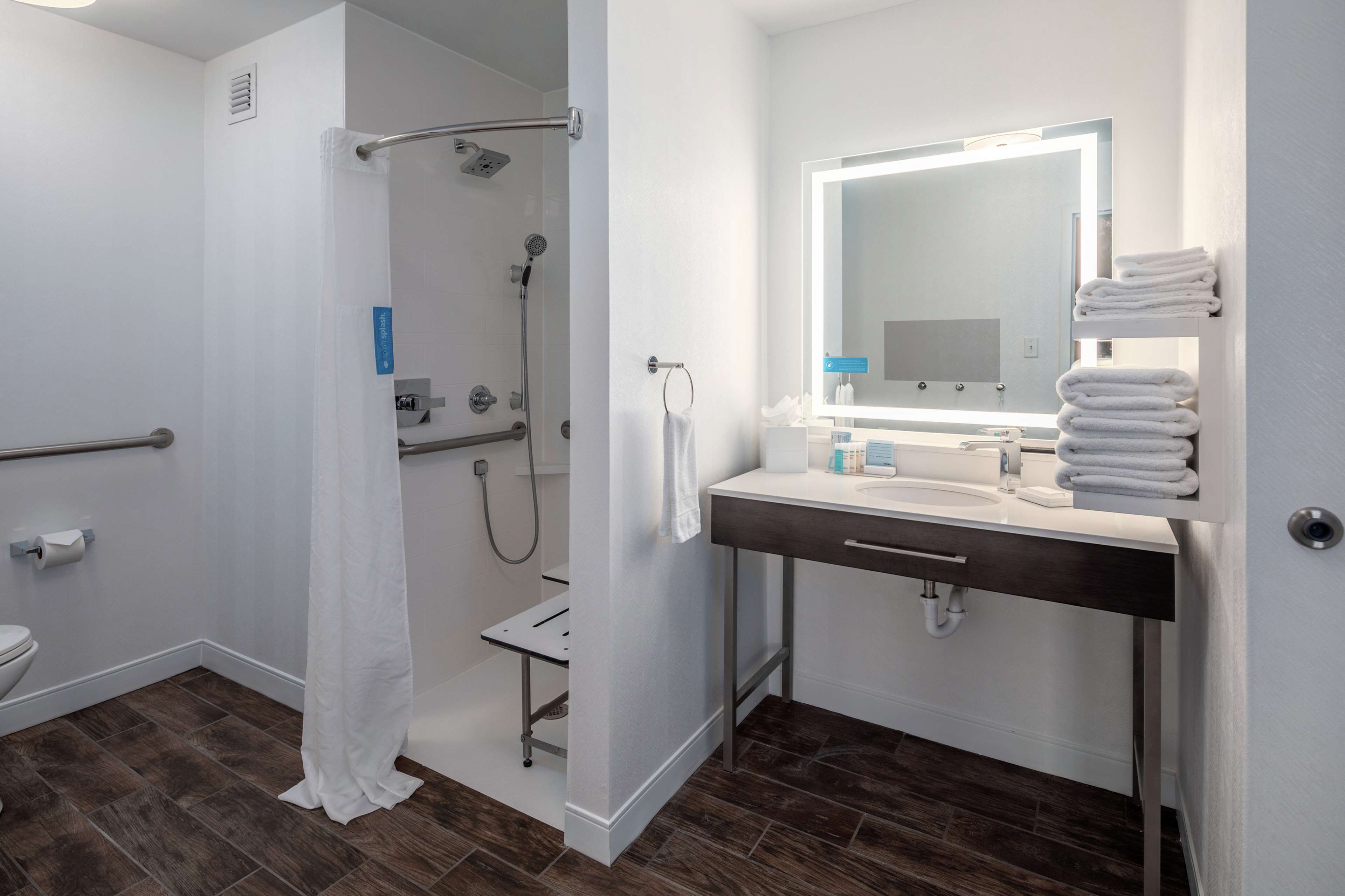 Un baño moderno con ducha, inodoro y tocador con espejo y perchero.