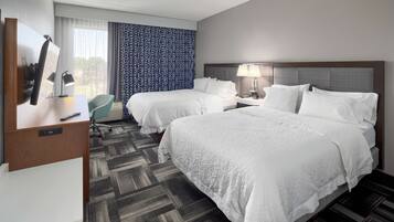 A hotel room with two beds, a desk with a chair, a TV, and a window with curtains.