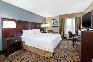 Una habitación de hotel con una cama grande, un escritorio con computadora, televisión y una silla.