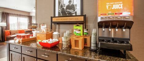 A breakfast bar with a juice dispenser, a framed photo, and various breakfast items.