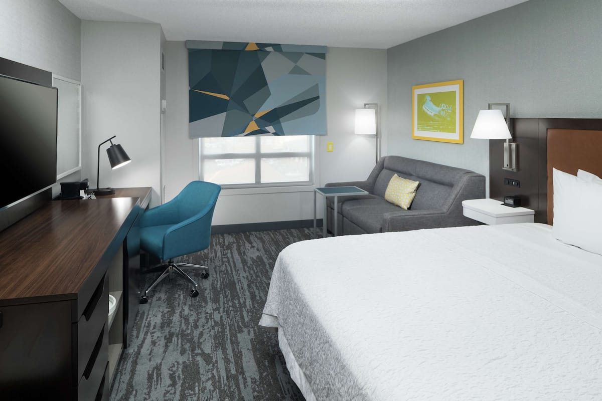 Una habitación de hotel con cama, escritorio con computadora, silla, mesita y ventana.