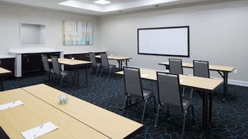 A conference room with tables, chairs, a projector screen, and a carpeted floor.