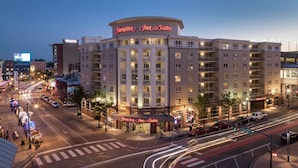 Edifici d'un Hampton Inn & Suites amb un senyal ben visible, situat en una intersecció urbana amb trànsit.