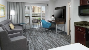 Habitació d'hotel amb un sofà gris, una cadira blava, escriptori amb televisió i zona de cuina amb microones.