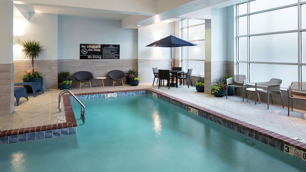 Una piscina interior amb senyal de socorrista, seients al costat de la piscina i plantes en testos.