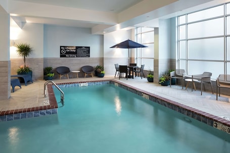 An indoor swimming pool with a lifeguard sign, poolside seating, and potted plants.