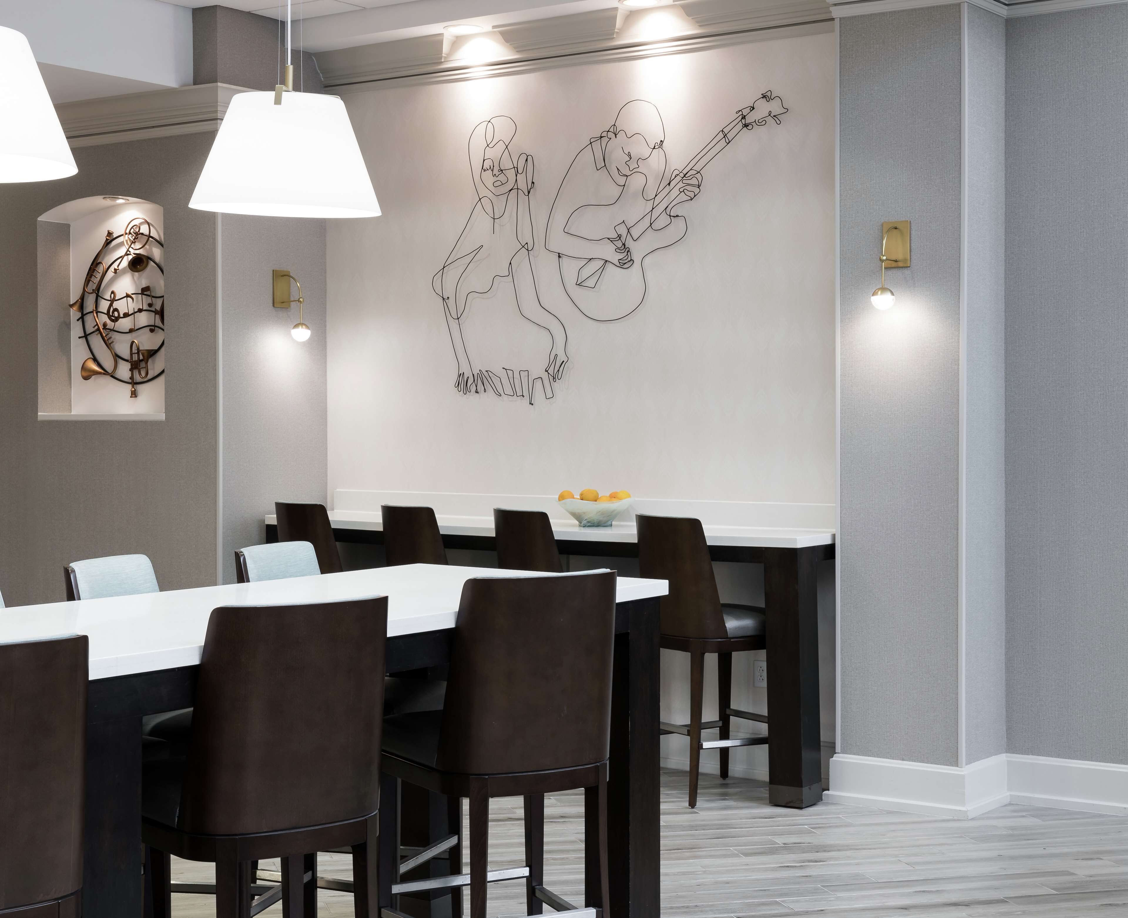 A modern dining area with a white table, dark chairs, and a wall art of two people playing guitars.