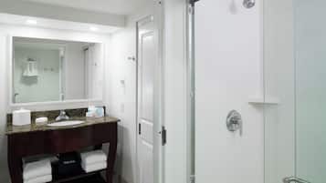 Un baño moderno con lavamanos de granito, un espejo grande y ducha con mampara de vidrio.