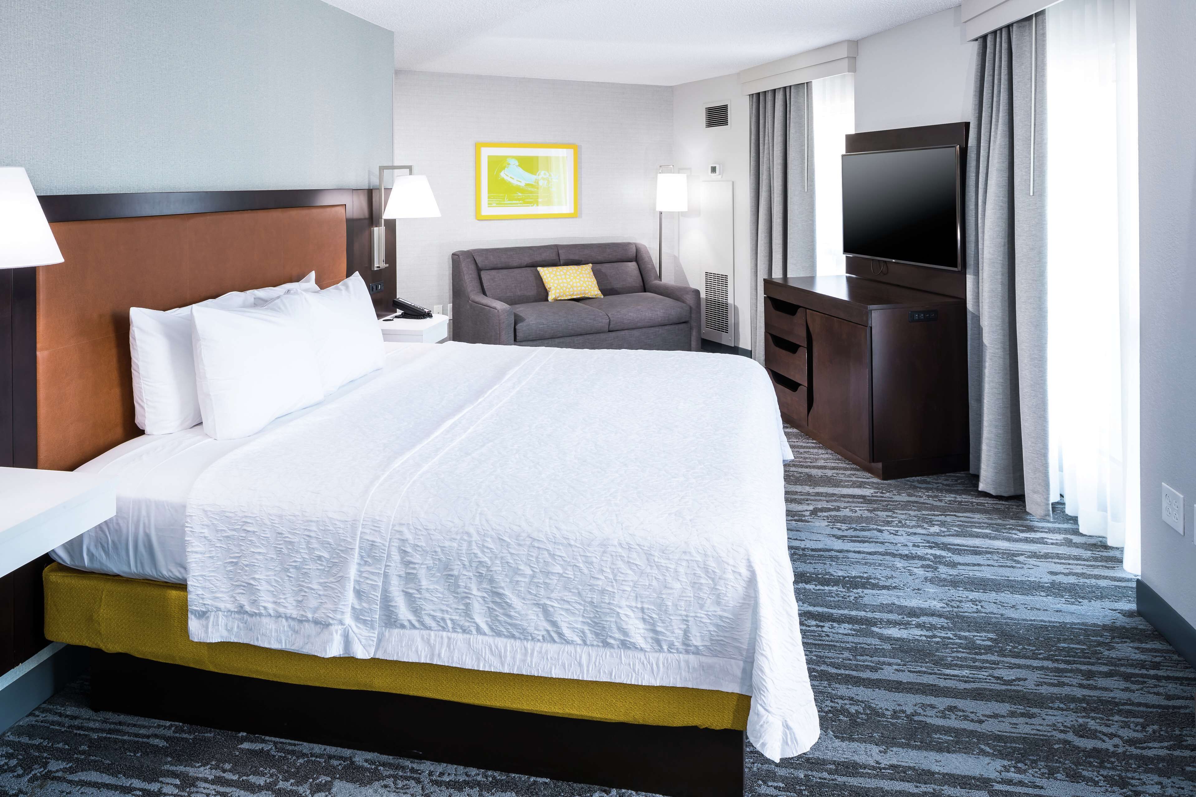 A hotel room with a large bed, a sofa, a TV, and a desk.
