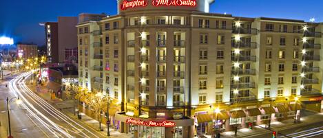 A Hampton Inn & Suites hotel with a prominent sign, multiple balconies, and a well-lit facade.