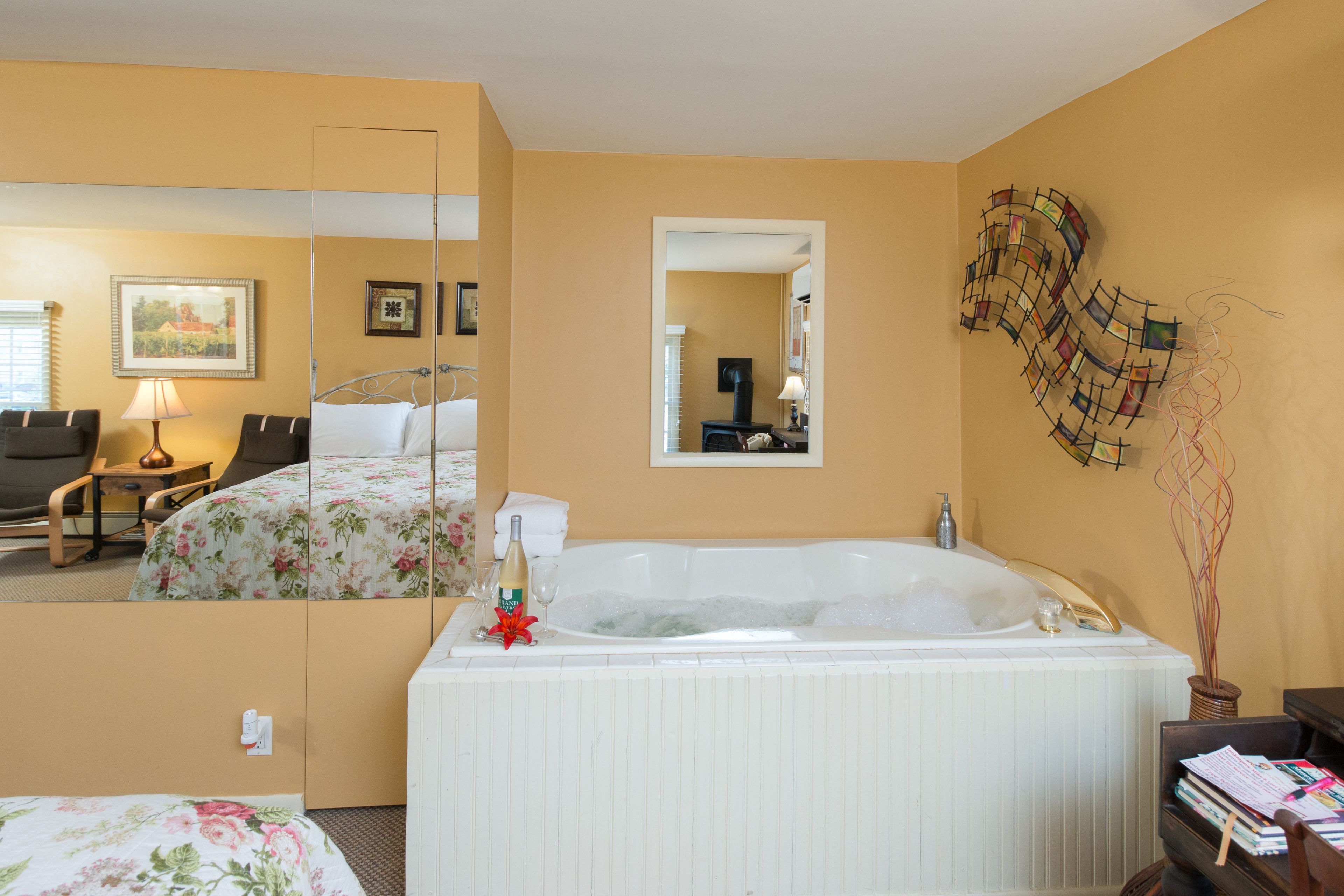 Una camera d'albergo con uno specchio grande, una vasca da bagno, un letto con biancheria da letto floreale, una scrivania con una lampada e una sedia.