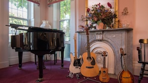 A grand piano, three guitars, and a fireplace in a room with large windows and a carpeted floor.
