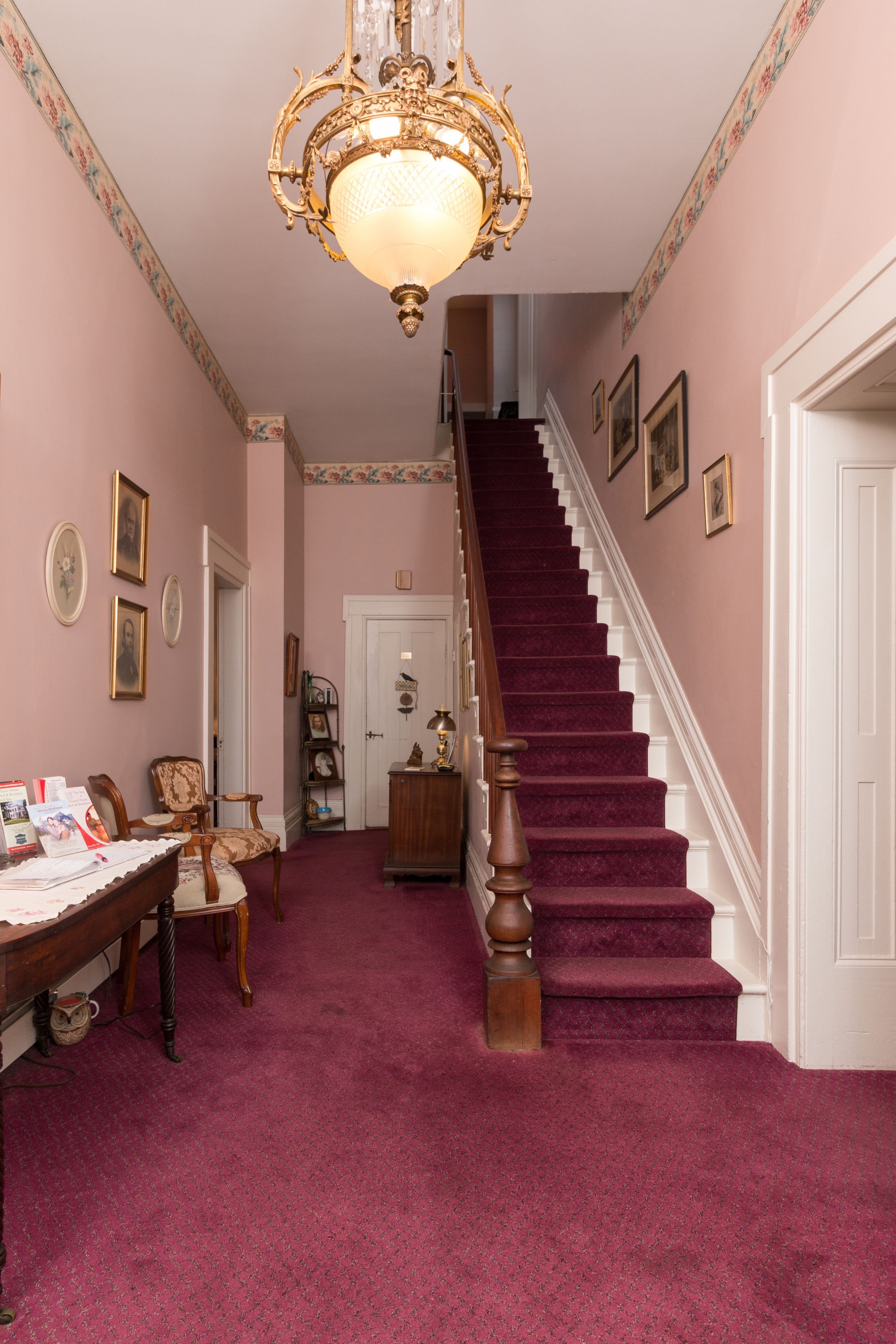 A staircase with a red carpet leading to a door, a chandelier, and framed pictures on the walls.