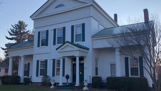 A two-story white house with green trim and a gabled roof.
