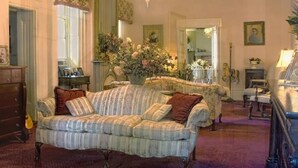 A cozy living room with a striped sofa, a wooden dresser, and a large floral arrangement.