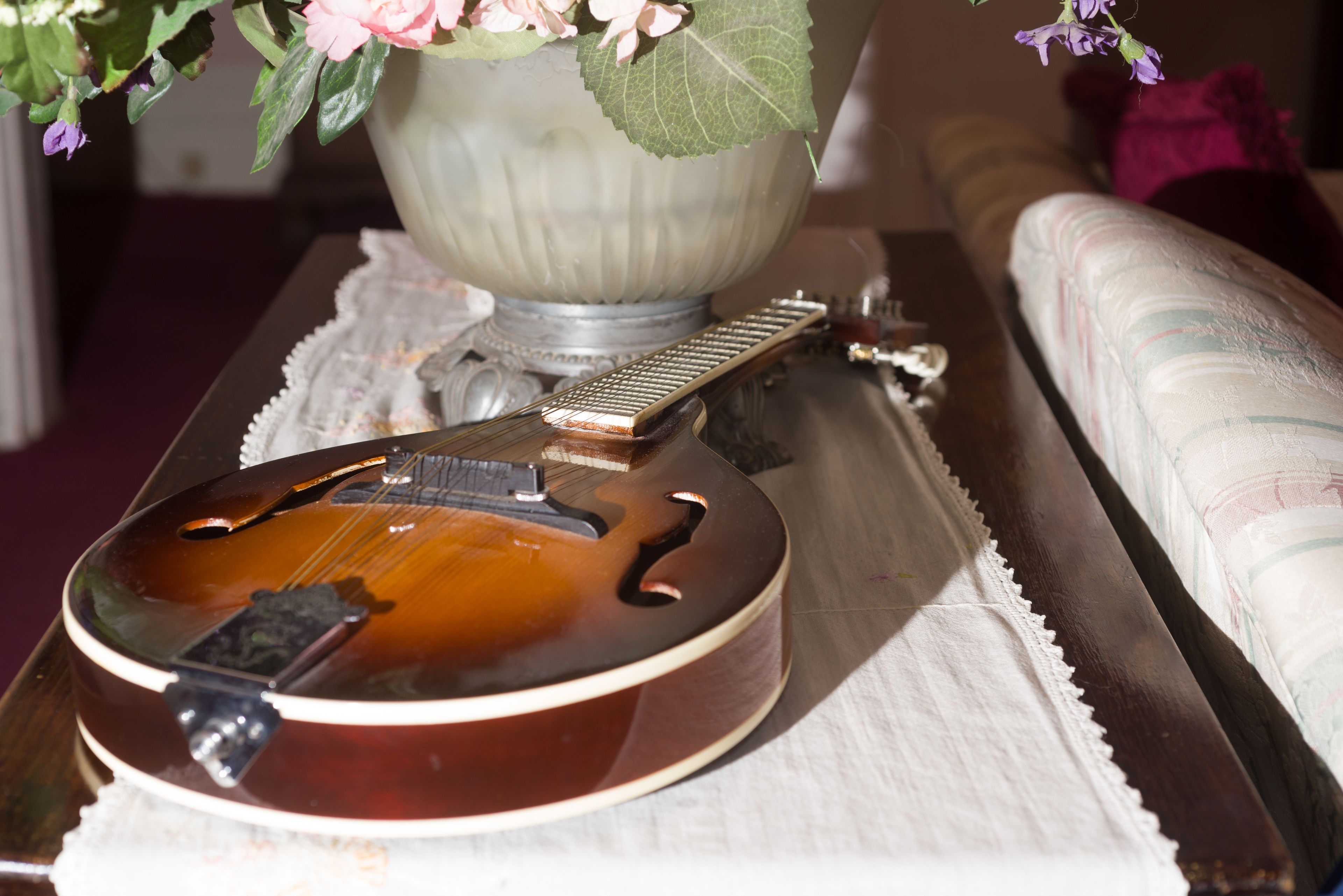A guitar on a table with a decorative lamp and a cushion in the background.