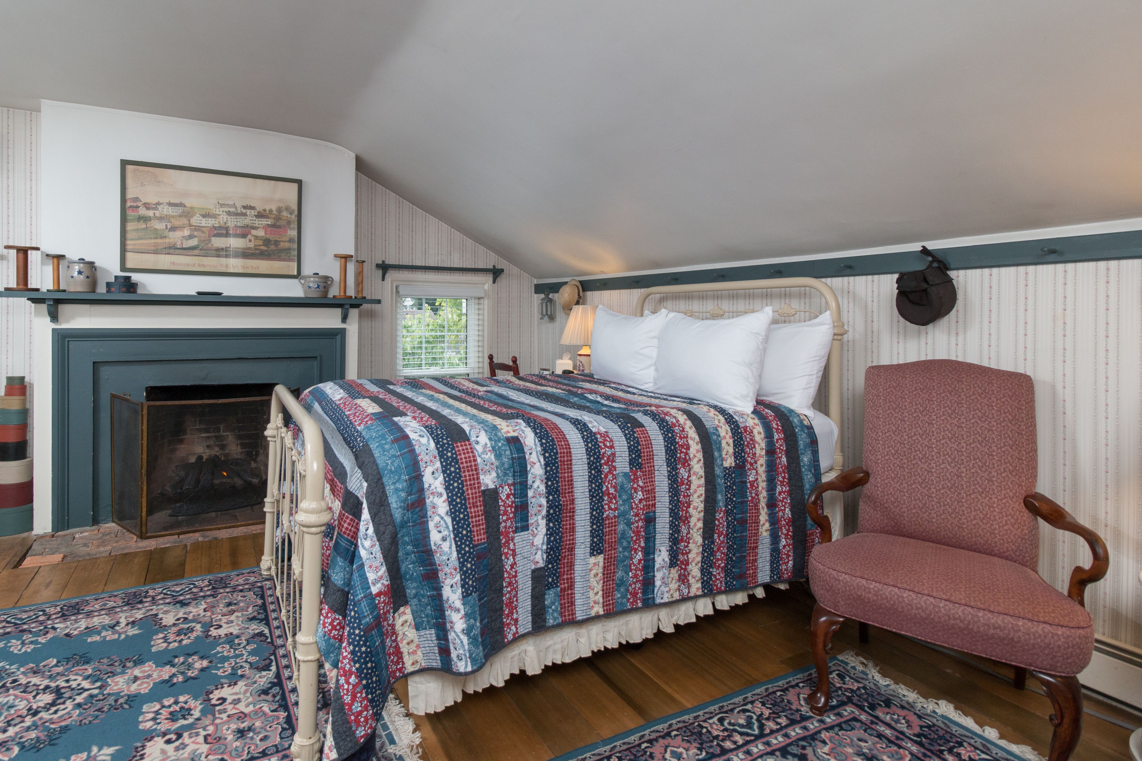 A bedroom with a bed, a chair, a fireplace, and a rug.