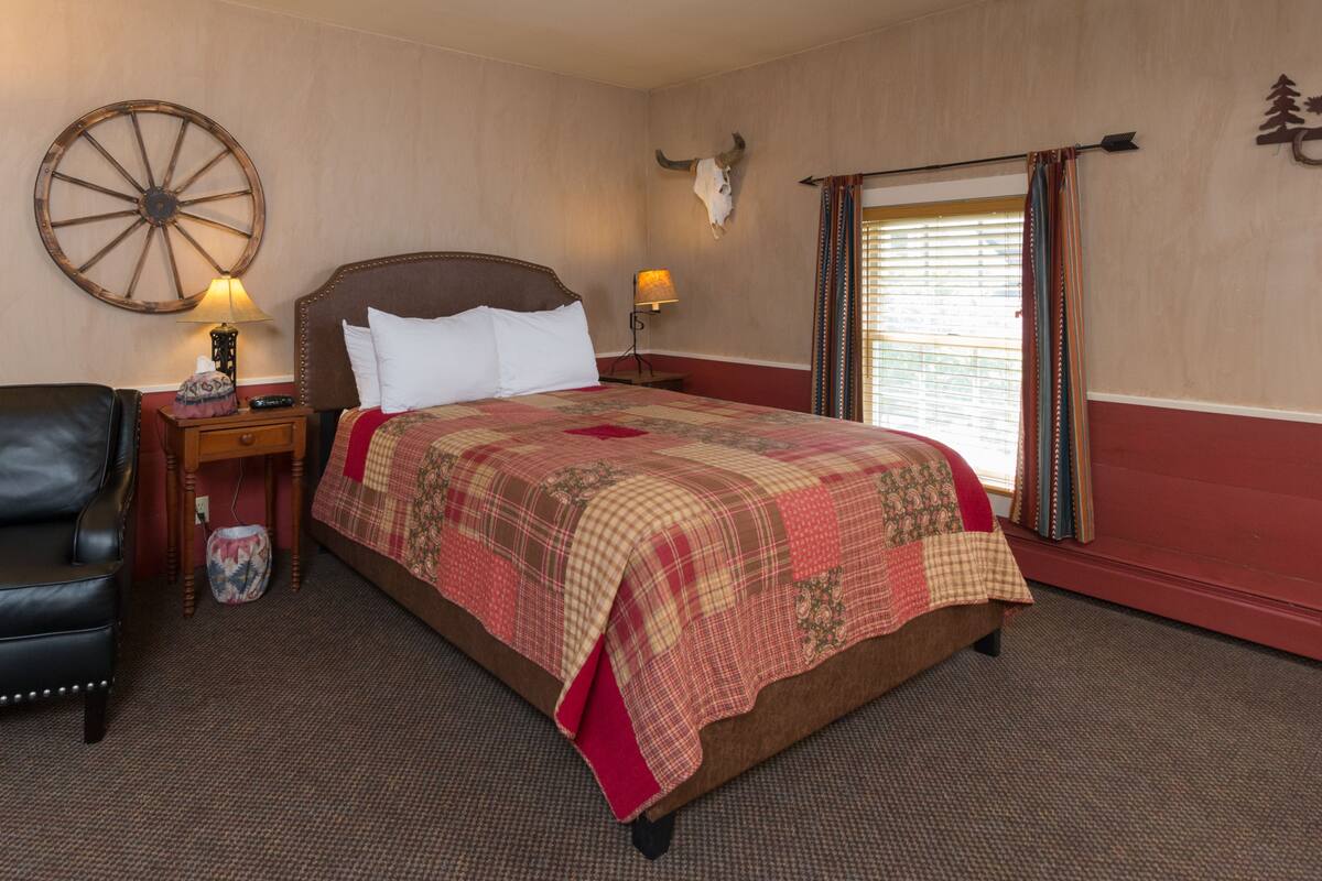 Ein Schlafzimmer mit einem großen Bett, einem Holzkopfstück, einem Nachttisch mit Lampe, einem Ledersessel und einer Wanduhr.