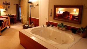 A bathroom with a large bathtub, a wooden cabinet, a mirror, and a small table with a lamp.