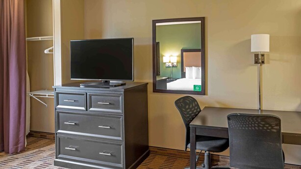 Ein Hotelzimmer mit Flachbildfernseher auf einem Schminktisch, einem Schreibtisch mit Stuhl, einem Spiegel an der Wand und einer Lampe.