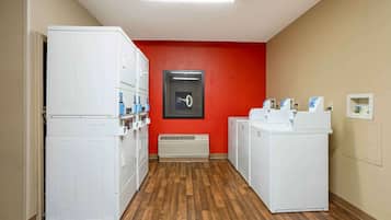 A laundry room with stacked washers and dryers, a red accent wall, and a vent.