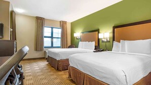 Ein Hotelzimmer mit zwei Betten, einem Schreibtisch, einem Sessel, einem Fernseher und einem Fenster mit Vorhängen.