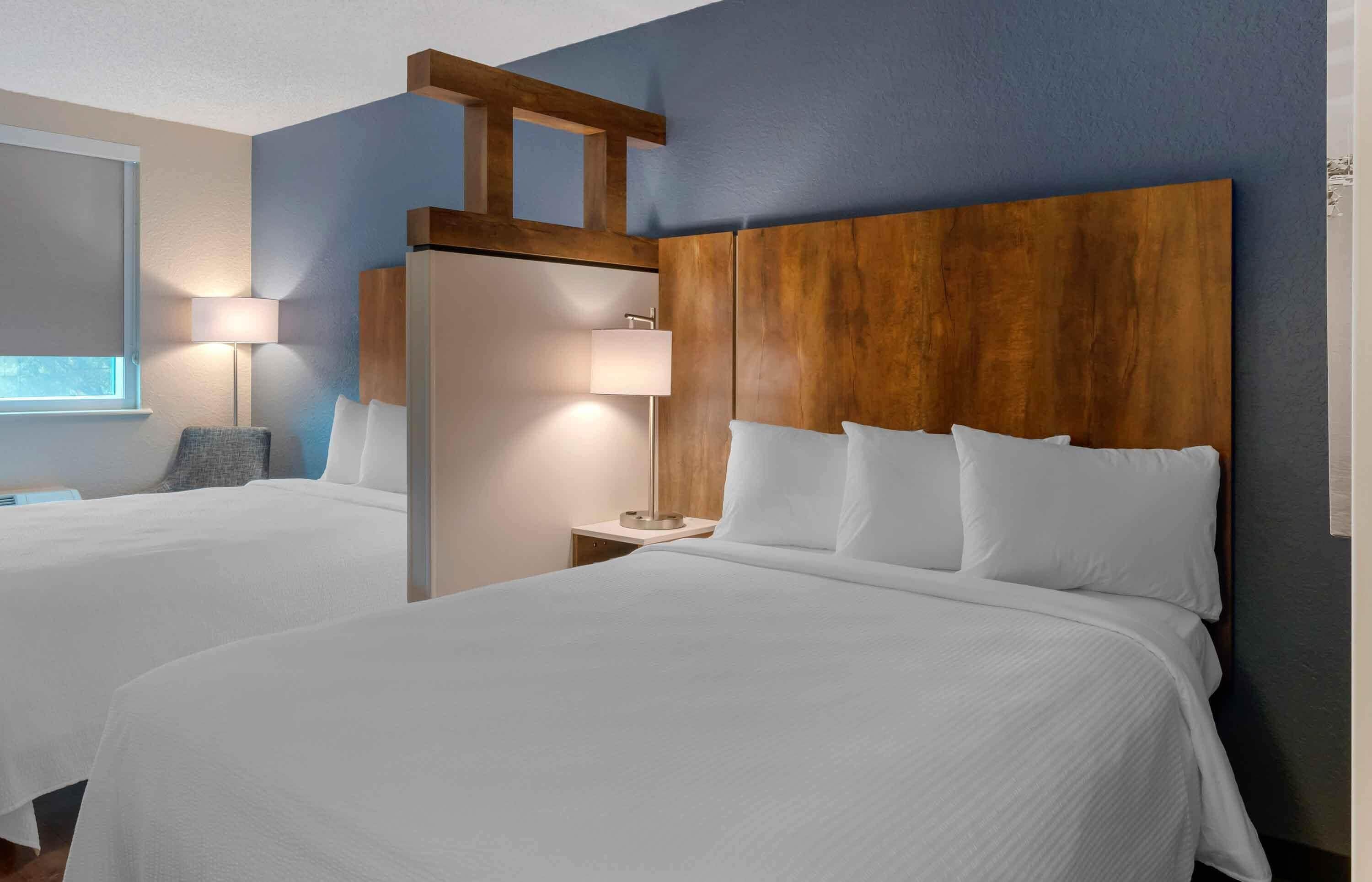 A hotel room with two beds, wooden headboards, bedside lamps, and a large window.