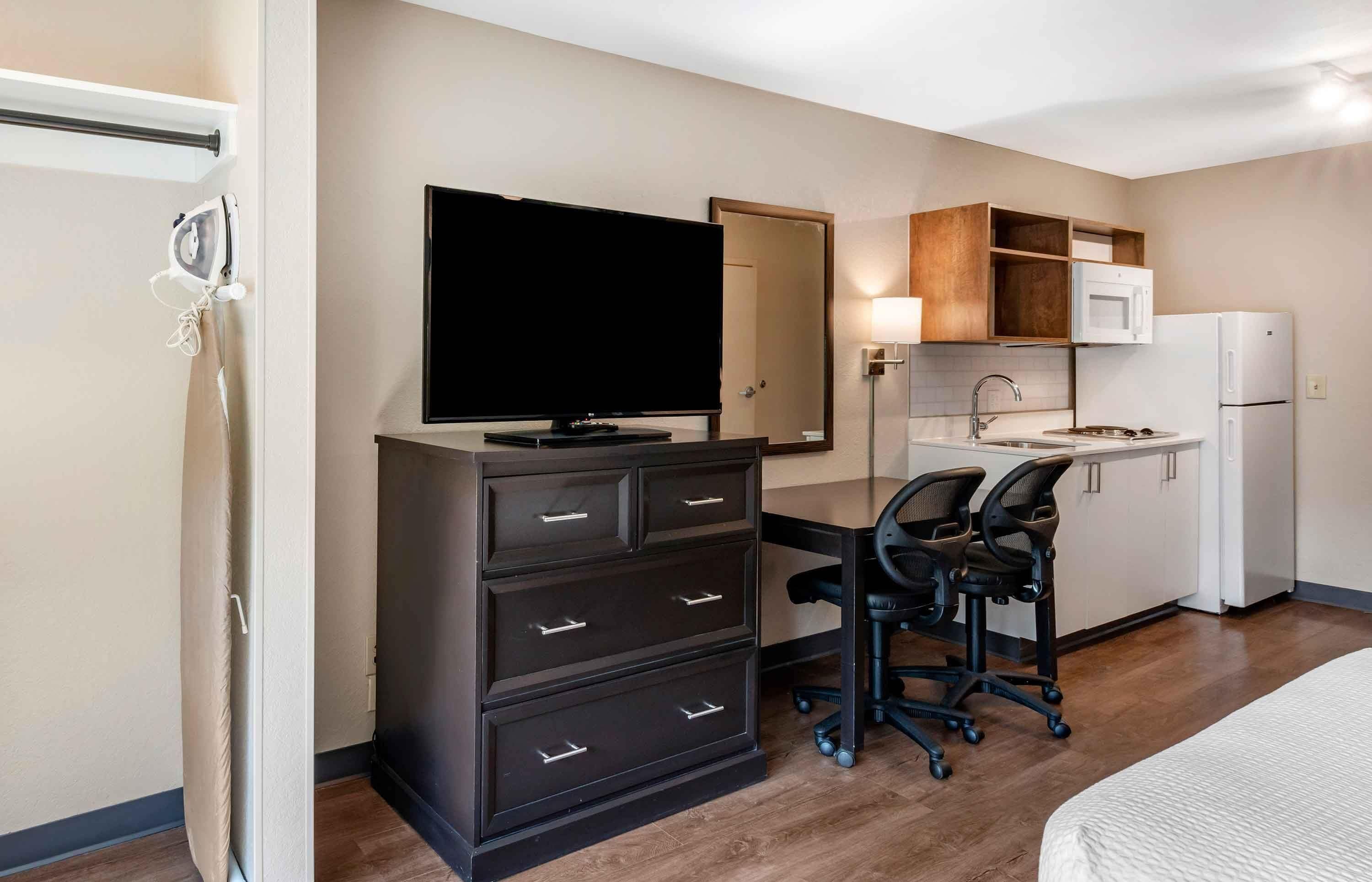 Ein Hotelzimmer mit Bett, Schreibtisch mit Stuhl, Fernseher, Mikrowelle, Kühlschrank und einer kleinen Küchenzeile.