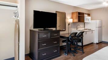 Ein Hotelzimmer mit Bett, Schreibtisch mit Stuhl, Fernseher, Mikrowelle, Kühlschrank und einer kleinen Küchenzeile.