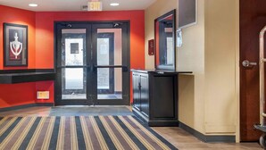 A hotel lobby with a red wall, a black door with glass panels, a striped carpet, and a framed picture on the wall. - Extended Stay America Suites Pittsburgh Monroeville (Monroeville)