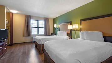 Habitación de hotel con dos camas, televisión, escritorio y ventana con cortinas.