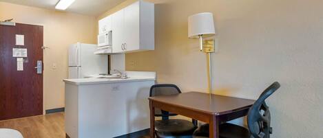 Une cuisine compacte équipée d’un réfrigérateur, d’un four à micro-ondes et d’un petit îlot central. On y trouve une table à manger avec deux chaises et une lampe.