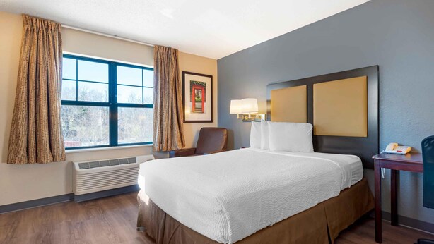A hotel room with a large bed, a chair, a desk with a lamp, and a window with curtains. - Extended Stay America Suites Pittsburgh Monroeville (Monroeville)