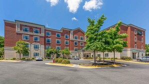 A multi-story hotel with a brick facade, a central courtyard with trees, and a parking lot. - Extended Stay America Suites DC Fairfax Fair Oaks Mall (Fairfax)