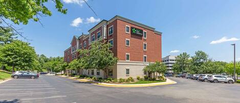A Stay America hotel with a brick facade, multiple windows, and a parking lot with several cars.