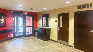 A hotel lobby with an exit sign, a trash bin, and a door with a mirror.