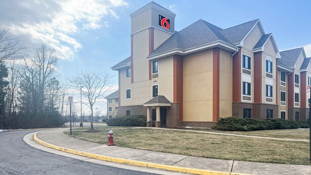 A multi-story hotel with a prominent '6' sign on the roof, a fire hydrant in front, and a well-maintained lawn. - Studio 6 – Chantilly, VA – Washington Dulles Airport (Chantilly)
