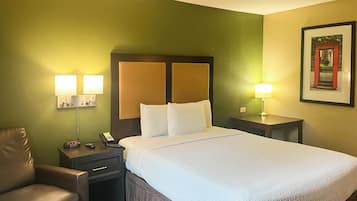 Habitación de hotel con una cama, dos lámparas de noche, una silla, una mesita de noche y un cuadro en la pared.