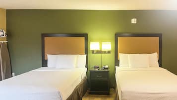 A hotel room with two beds, a nightstand with lamps, and a wall-mounted alarm clock.