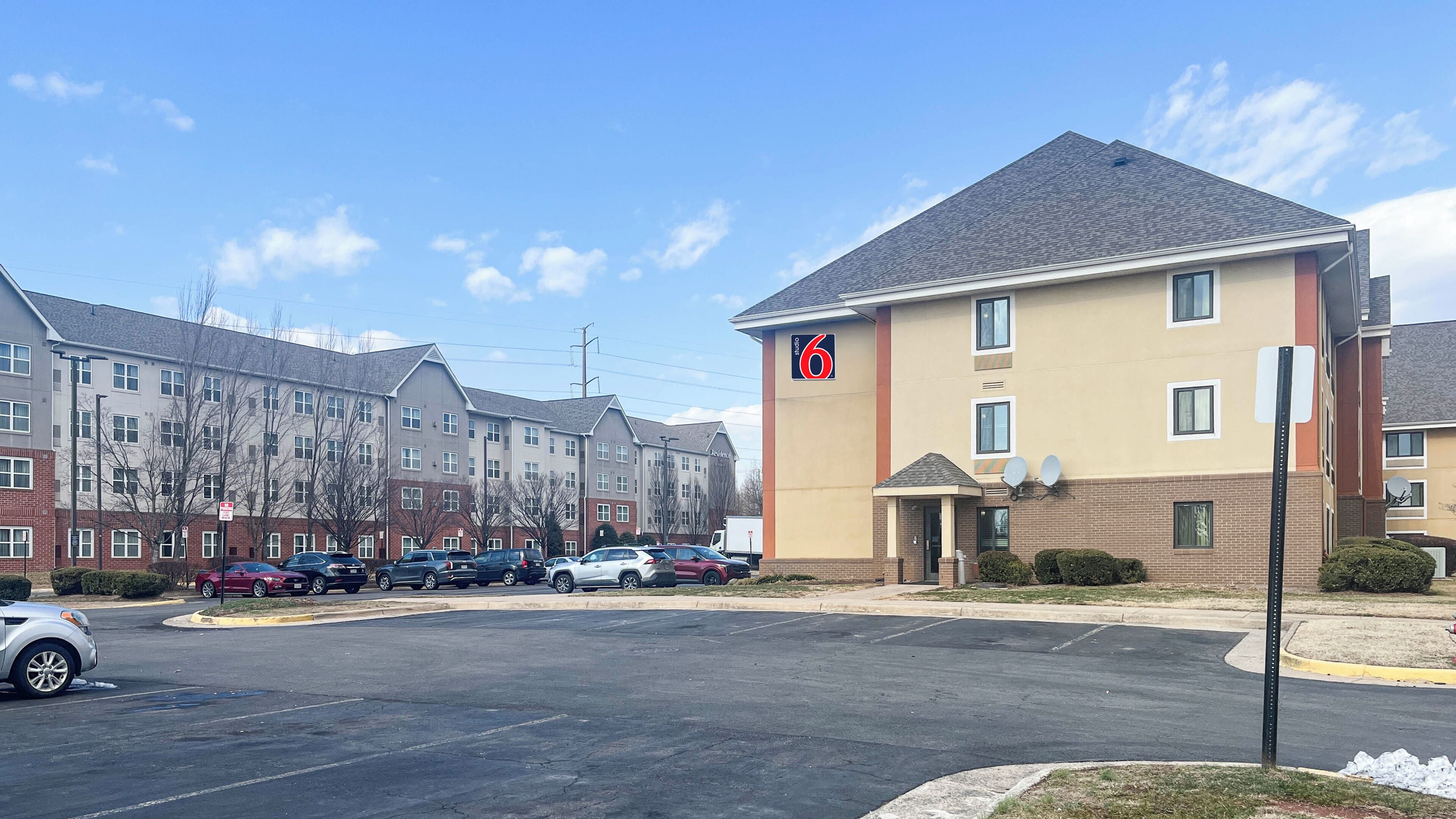 A multi-story hotel with a parking lot in front, featuring a prominent '6' sign on the building.