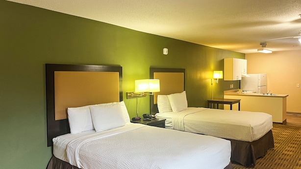 A hotel room with two beds, a desk, a lamp, a phone, and a kitchenette.