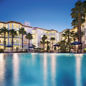 A hotel with a swimming pool, palm trees, and outdoor seating areas.