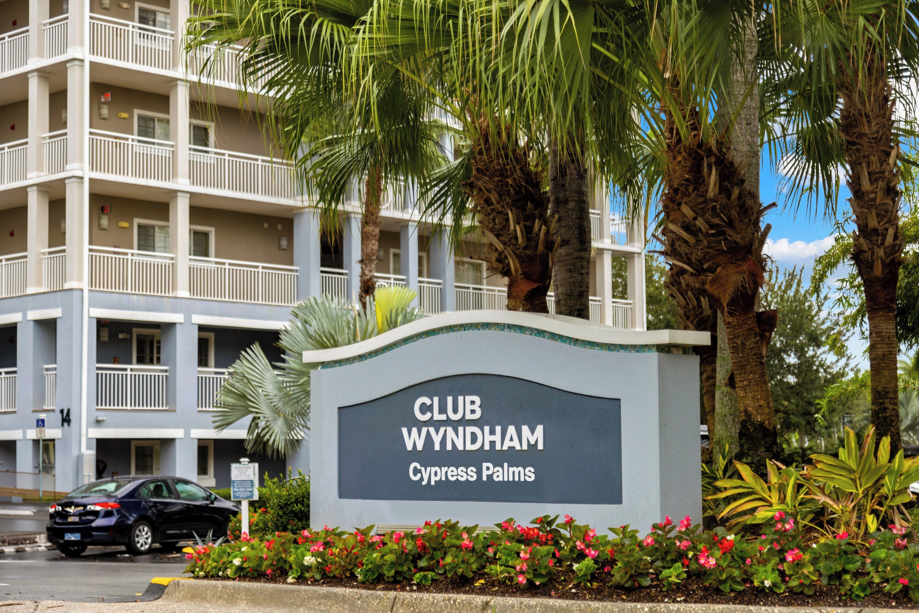 A sign for Club Wyndham Cypress Palms with a multi-story building in the background.